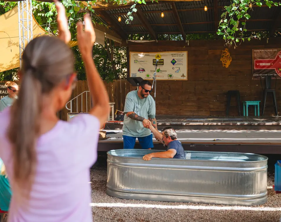 A baptism in a stock tank, with people gathered around